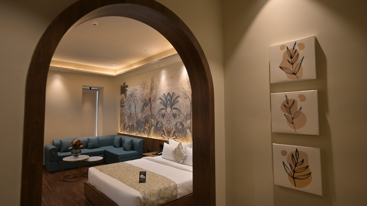 A view through an arched doorway revealing a bed, seating area, and decorative wall art, complemented by three framed pictures on the wall on the outside in Premium Room. - Clarks Safari Haridwar