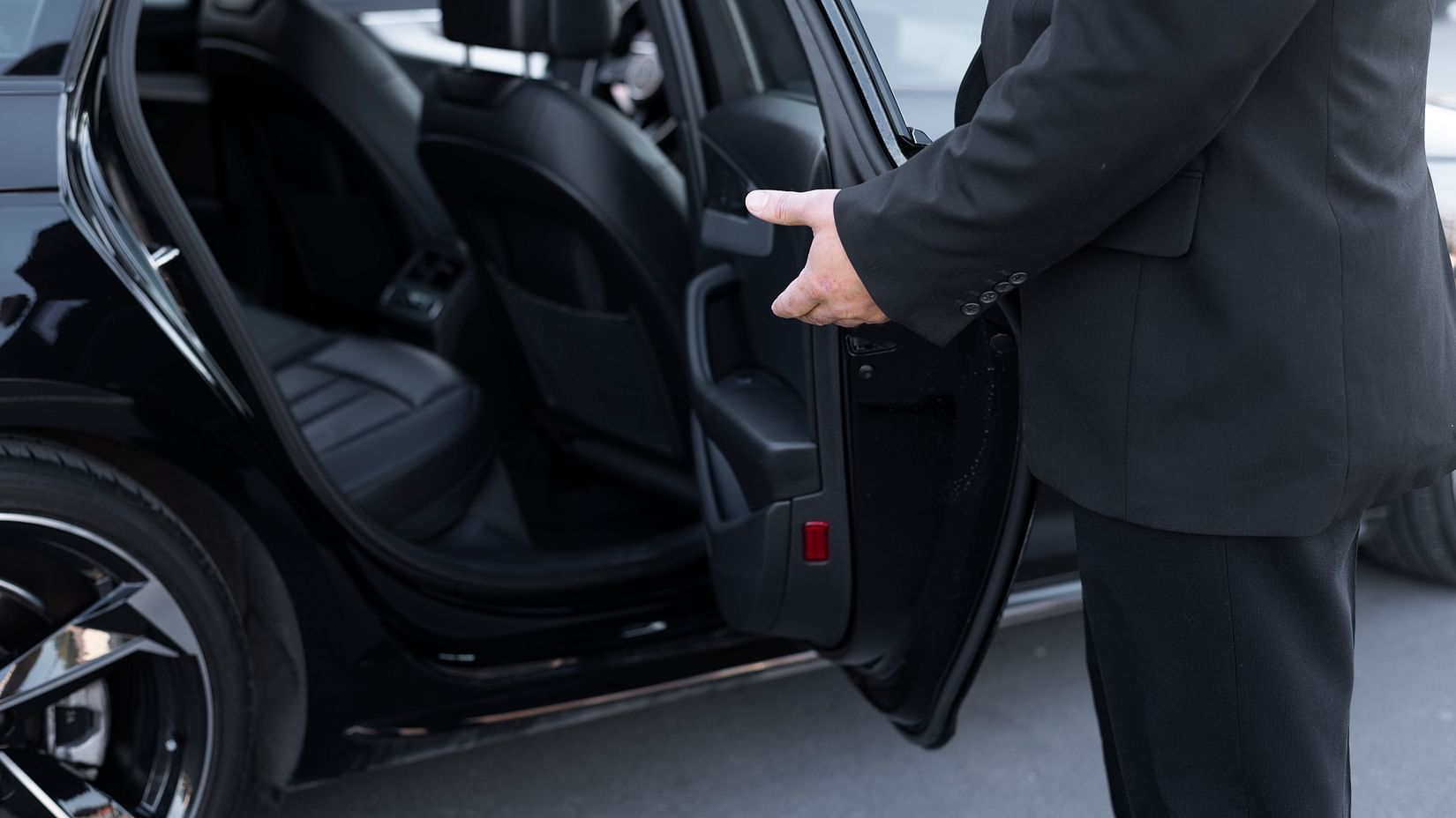 Chauffeur in a black suit holding open the rear door of a luxury car.