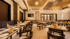 A well-lit dining room with rows of wooden tables and chairs under an elegant decorative ceiling at Ananta Express, Katra.