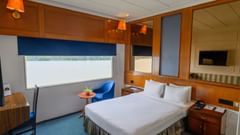 Polo Floatel Kolkata bedroom with a large bed, blue chair, and desk, offering a view of the water from the window.