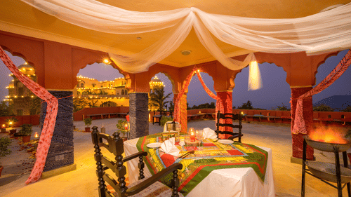 A dining setup at Tijara Fort-Palace during the evening with a table for two displaying cutlery kept on a patterned table runner