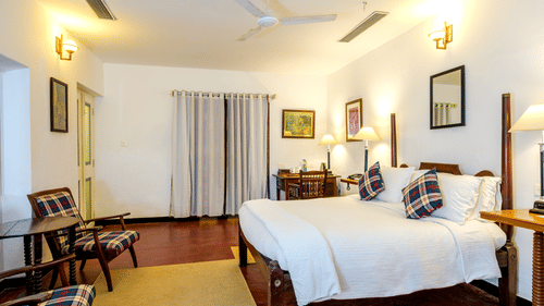 A room featuring a plush bed with linens and cushion with a seating space in front of it under warm lighting at The Tower House - 17th Century, Cochin