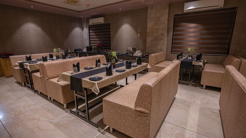 The lounge-style seating area with cushioned arm sofas, tables wit neatly arranged plates, spoon, glass and elegant lighting at Clarks Collection Somnath.