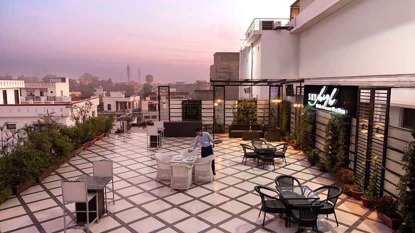  A rooftop terrace offering a stunning view of the city, with comfortable outdoor seating and a tranquil setting with a  man  fixing things on the table - Clarks Inn Express, Near Jammu Bari Brahmana Railway Station