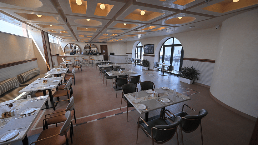 A brightly lit, spacious restaurant dining area with tables set for service. - Clarks Safari Haridwar