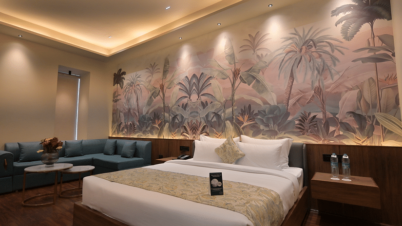 Premium Room featuring  a king size bed with white linens and a patterned throw, a blue corner sofa, and a large mural of a jungle scene on the wall behind the bed. - Clarks Safari Haridwar