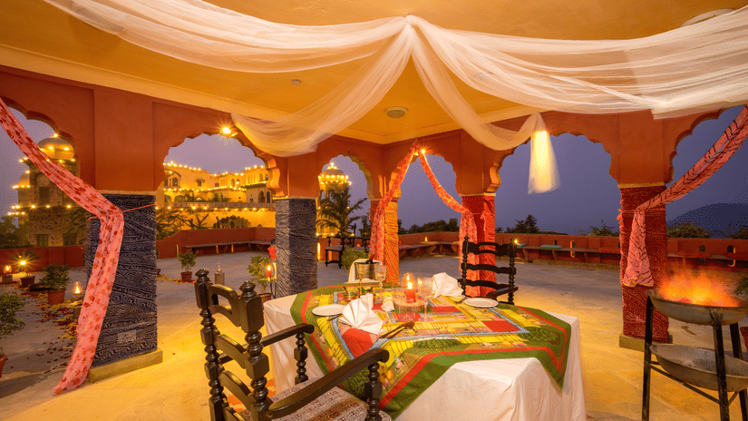 A dining setup at Tijara Fort-Palace during the evening with a table for two displaying cutlery kept on a patterned table runner