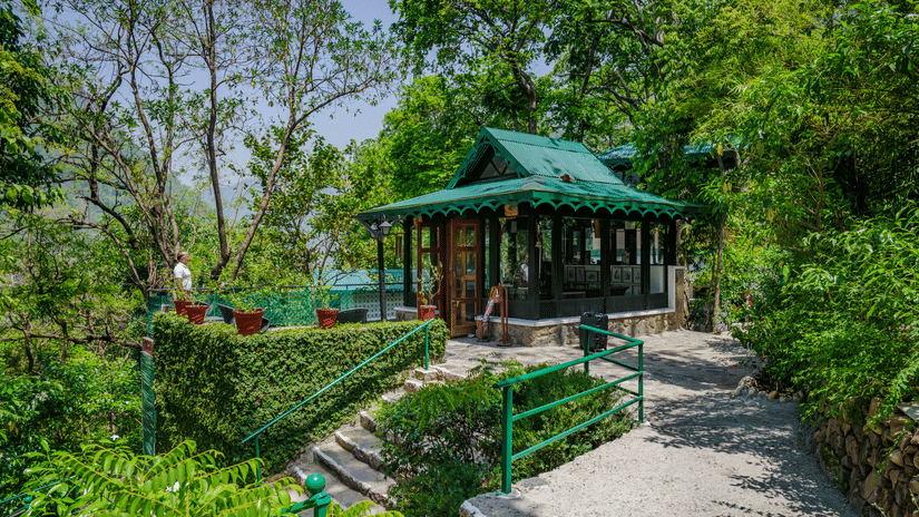 A roofed area surrounded by lush greenery and paved pathways at Neemrana's Glasshouse on The Ganges.