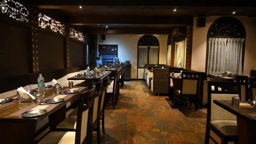 Restaurant interior with rows of dining tables, chairs, table settings, and ambient lighting.