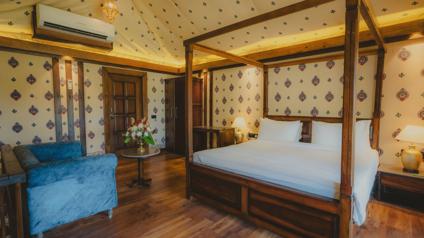 A Premium Duplex Tent bedroom featuring a sofa, a poster bed, bedside table with lamps on either side, cabinet table, a wardrobe, and a centre table with flower vase at The Baagh Ananta Elite, Ranthambore