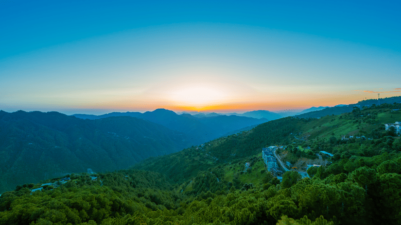  A breathtaking sunrise over forested mountains seen from The Manor Sports & Wellness Hotel, with a view of winding roads and lush green valleys.