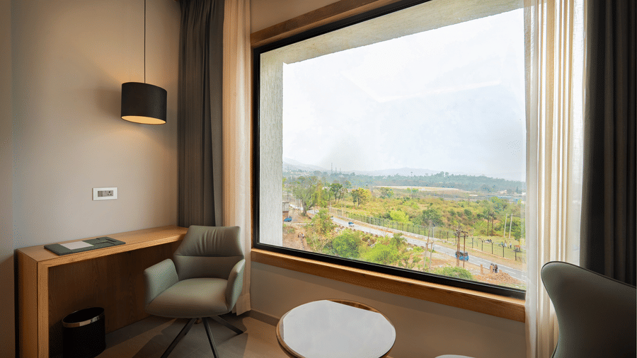 A modern bedroom corner featuring a green armchair and a large window overlooking a lush landscape at Ananta Express, Katra.
