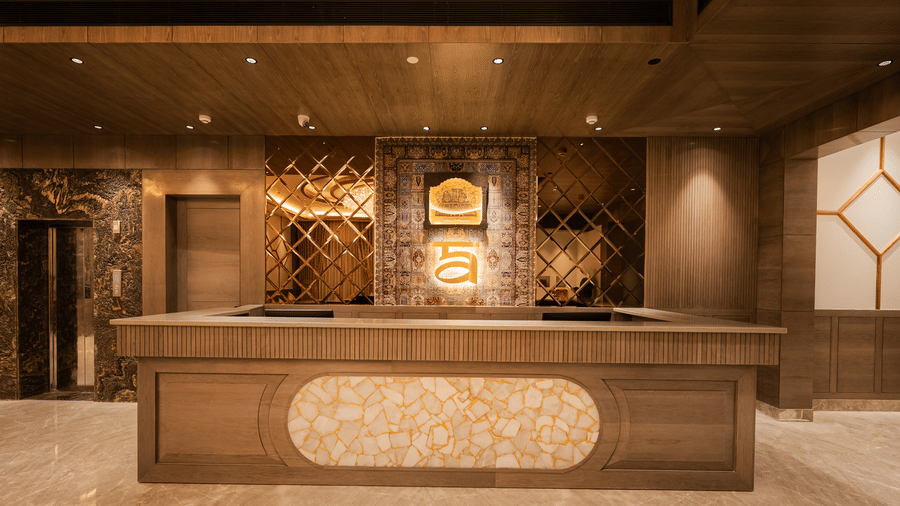 A large wooden and marble reception desk illuminated by warm lighting in the main lobby at Ananta Express, Katra.