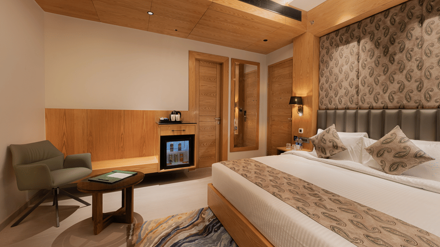 A guest room featuring a king-sized bed, a green armchair, and a wooden cabinet with a minibar at Ananta Express, Katra.