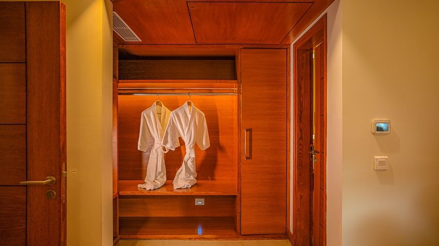 An open closet in a hotel room reveals hanging white robes and wooden shelves with folded towels. The closet is well-lit, and the interior is finished with wood - Ananta Spa and Resort, Pushkar