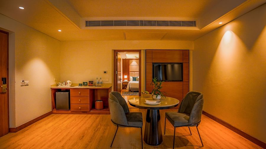A hotel room showcases a round wooden dining table with two chairs positioned near a doorway leading to another room. A small kitchenette area with a sink and counter is visible in the background - Ananta Spa and Resort, Pushkar