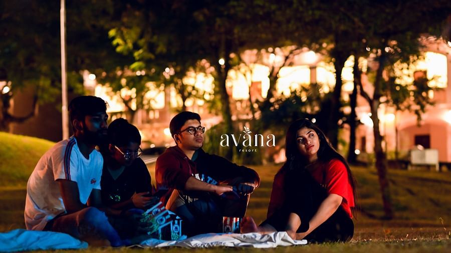 A group of people having a picnic or outdoor gathering in the evening, with warm lighting.