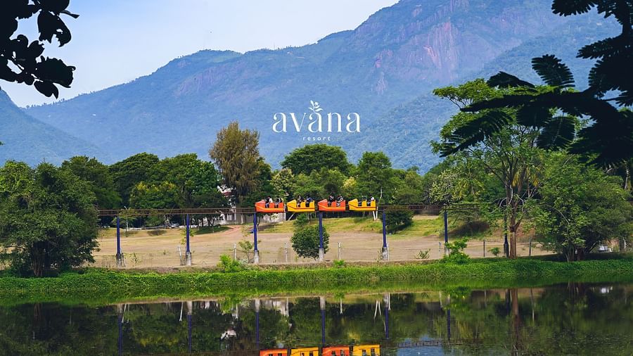 A scenic view of a resort or natural area with a lake, green hills, and buildings.