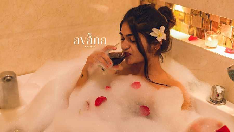 A person relaxing in a bathtub filled with bubbles and rose petals.