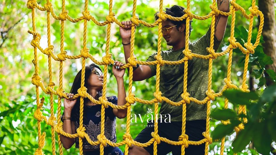 Two people climbing on a rope net structure in an outdoor adventure park.