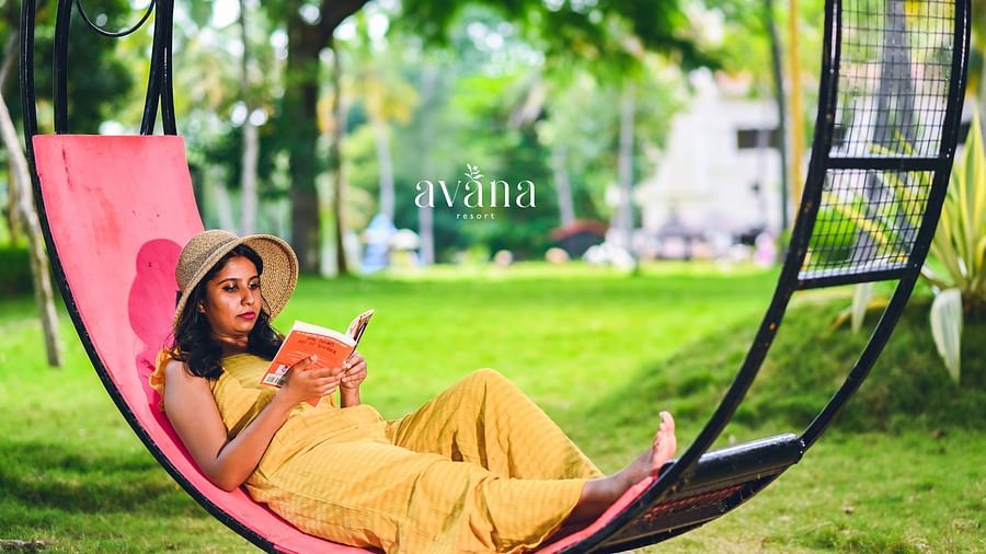 A person sitting in a swing, enjoying a drink, in a park-like setting.