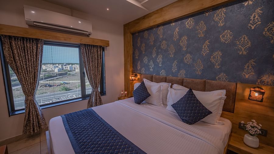 Spacious room with a double bed, ac, water bottles, bedside table with flower vase on the top and city view window at Clarks Collection, Somnath.