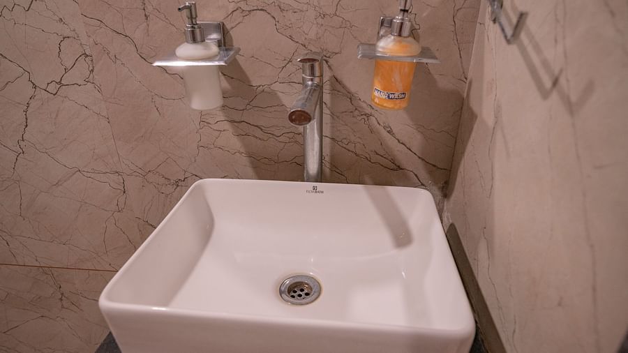 A bathroom with square sink with wall-mounted tap and soap dispenser on a beige marble wall at Clarks Collection Somnath .