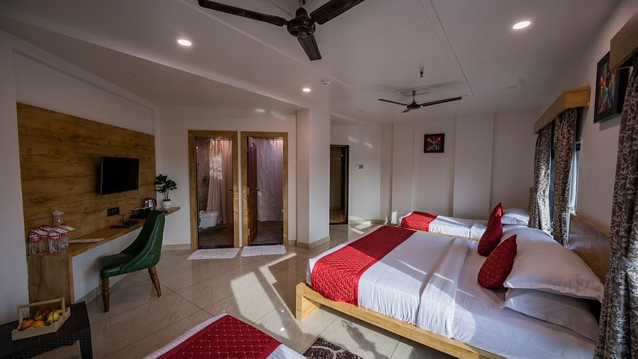 A room at Clarks Collection Somnath with beds, red runners, desk, tv, ceiling fan, chair, table and fruits on the table and wooden decor.
