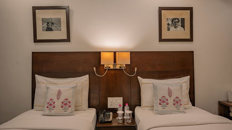 Twin beds with embroidered cushions, bedside phone, water bottles, frames, and soft lighting at Clarks Collection Vadodara.
