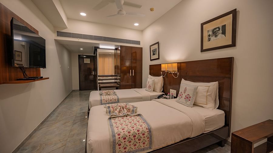 Room with two single beds, TV, wooden wardrobe, and framed photos at Clarks Collection Vadodara.