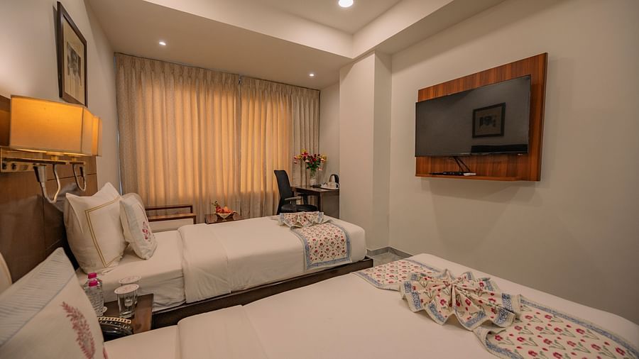 Wide view of twin beds, wall-mounted TV, desk with kettle and flower vase in the corner at Clarks Collection Vadodara.