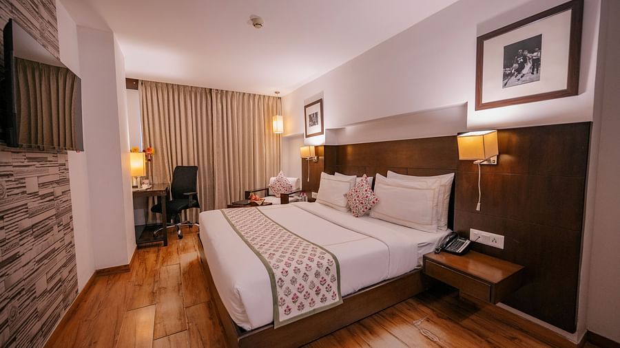 Wide view of the room showing the bed, armchair, lamps, curtains, and work desk with chair at Clarks Collection, Vadodara.
