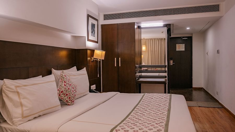 A room with double bed, wooden flooring, lamps, frame, remotes, wardrobe, and mirror at Clarks Collection, Vadodara.