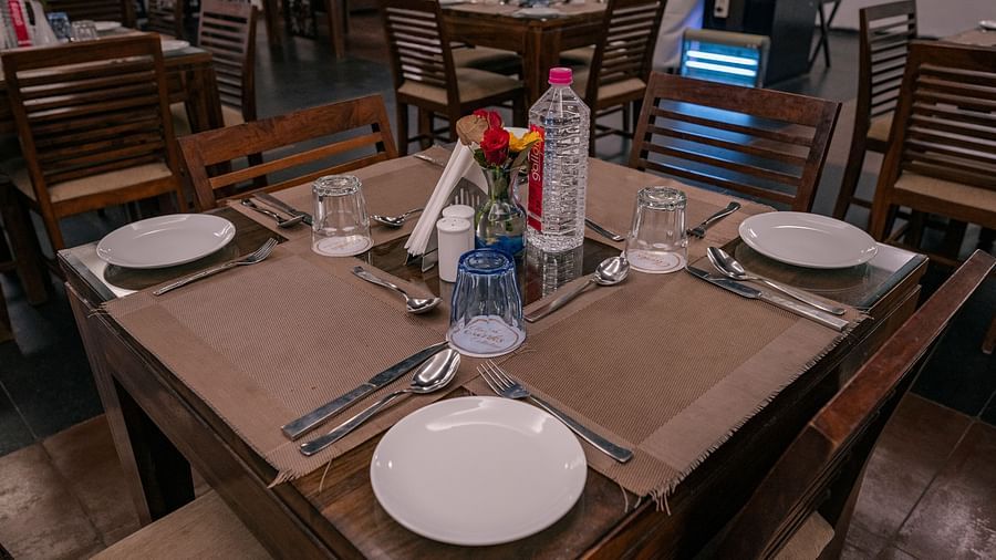 Close-up of a dining table set with plates, glasses, spoons and a flower vase at Clarks Collection, Vadodara.