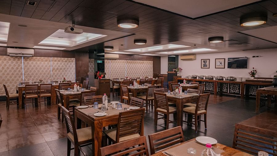 The dining area with wooden tables, chairs neatly arranged water bottles, spoons and plates at Clarks Collection, Vadodara.