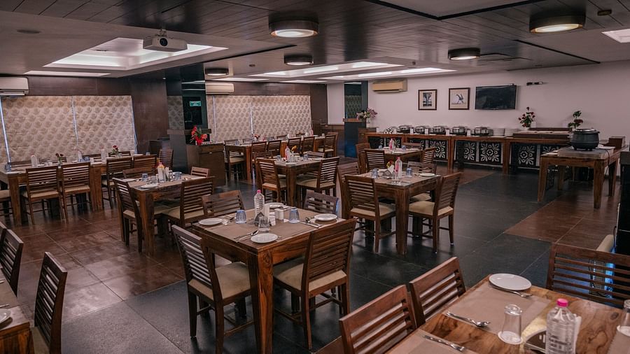 The dining area with wooden tables, chairs neatly arranged water bottles, spoons and plates at Clarks Collection, Vadodara.