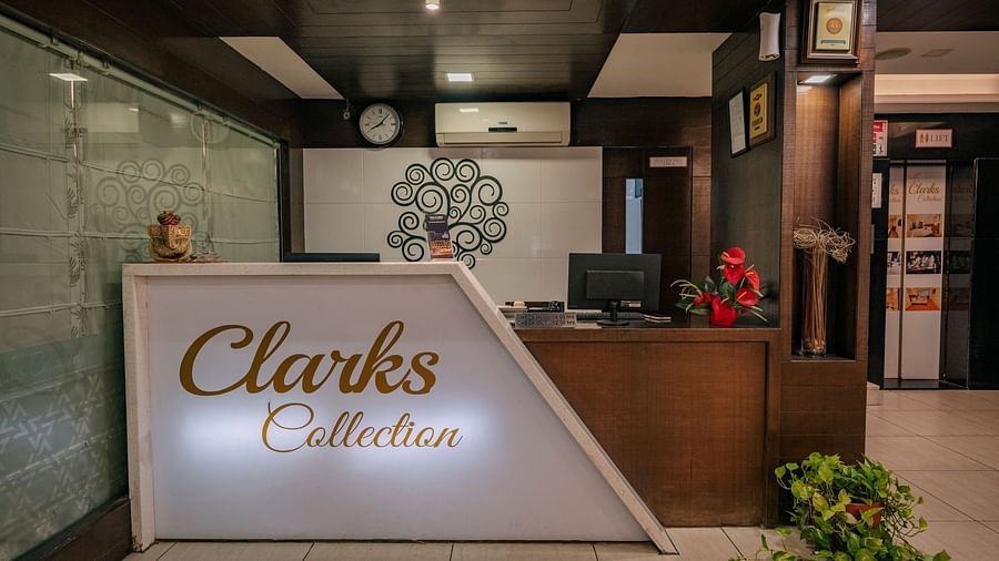 Reception area at Clarks Collection, Vadodara, featuring a white front desk with signage of Clarks Collection, a wall clock, desktop monitors, and indoor decorative plants.