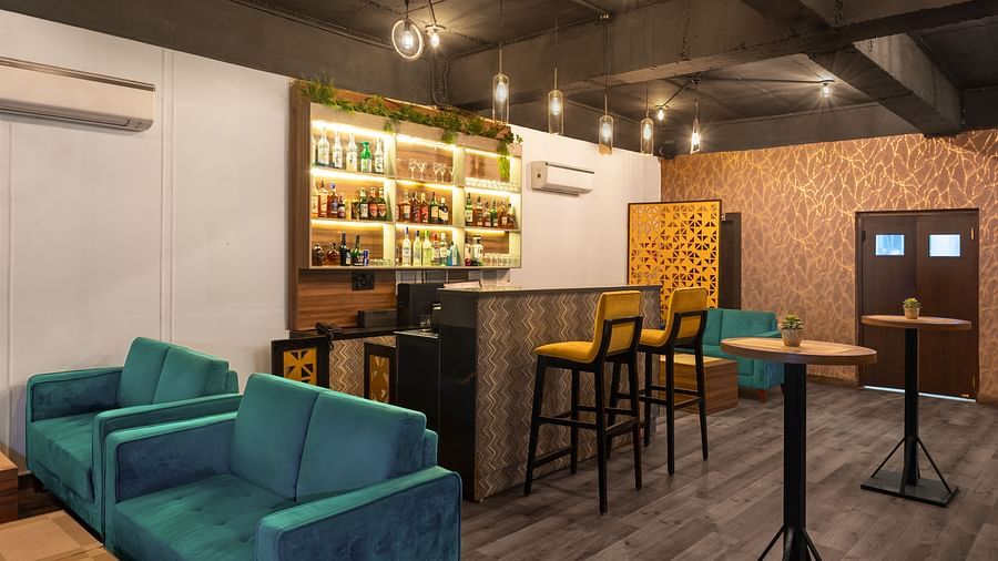  A cosy Bar lounge area with comfortable seating in teal and gold tones, perfect for relaxing and socialising with a wooden counter and compartments in the wall behind the counter with Glass bottle - Clarks Inn Express, Near Jammu Bari Brahmana Railway Sta
