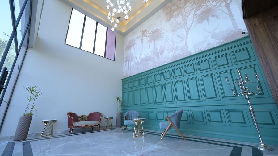 A spacious, high-ceiling event space with a teal panelled wall, minimalist furniture, and natural light coming through large windows. - Clarks Safari Haridwar