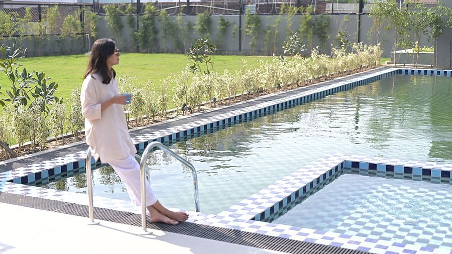 A person sitting on the edge of a swimming pool with a grassy area and trees in the background. - Clarks Safari Haridwar