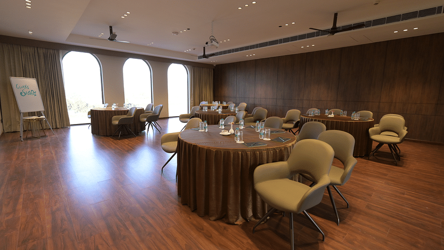 A meeting room set up with a round table and chairs, along with additional seating against the wall and natural light coming through arched windows. - Clarks Safari Haridwar