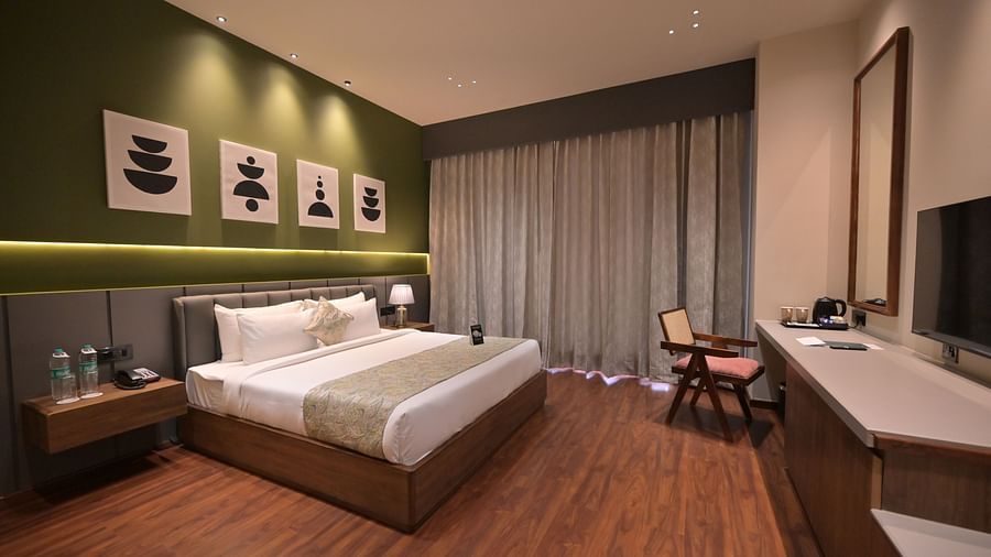 Deluxe Room featuring a king size bed with a grey and white runner, minimalist artwork on the wall, and wooden flooring.  - Clarks Safari Haridwar