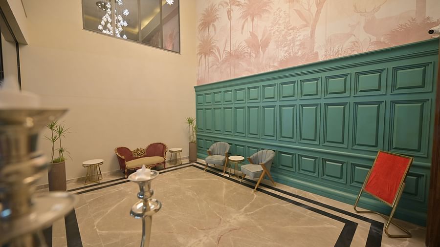 A brightly lit event space with a high ceiling, textured walls, and teal wainscoting, furnished with chairs and a small sofa. - Clarks Safari Haridwar