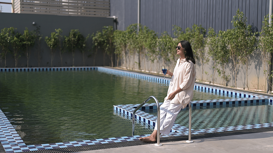 A woman holding a drink in her hand standing at the corner of a swimming pool on a bright sunny day. - Clarks Safari Haridwar