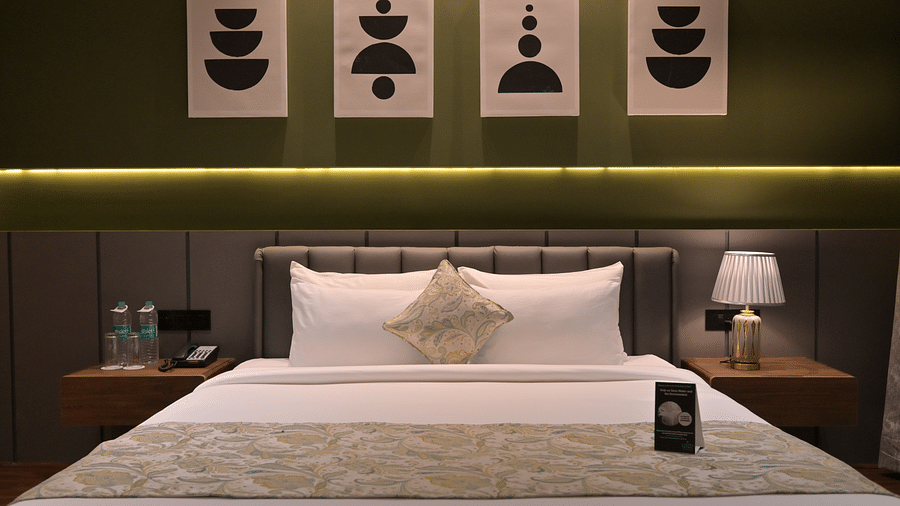 Deluxe Room with a neatly made bed, flanked by bedside tables and lamps, and decorated with four pieces of abstract art above the headboard. - Clarks Safari Haridwar