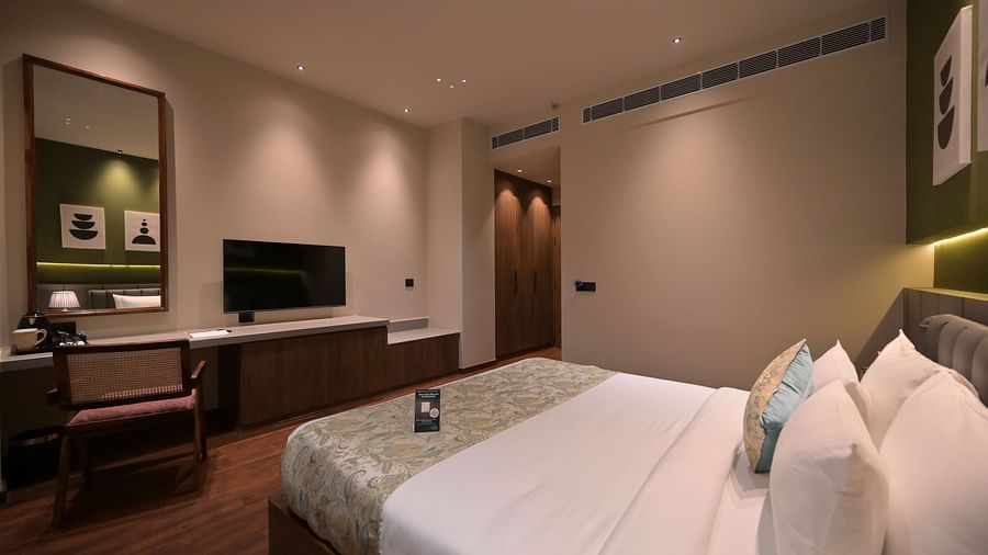 Deluxe Room with a king size bed, a desk area with a chair and television, and minimalist decor. - Clarks Safari Haridwar