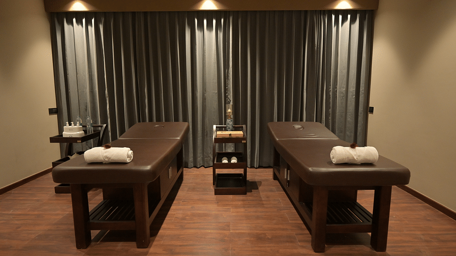 A spa treatment room is shown with two massage tables, rolled towels, and soft lighting. - Clarks Safari Haridwar