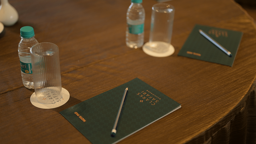 A close-up shows a wooden conference table with water bottles, glasses, notebooks, and pens arranged for a meeting. - Clarks Safari Haridwar