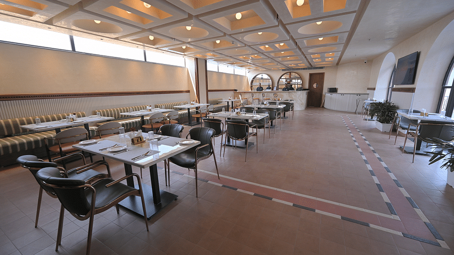 A well-lit, empty restaurant dining area with tables and chairs, featuring a patterned ceiling and carpet. - Clarks Safari Haridwar