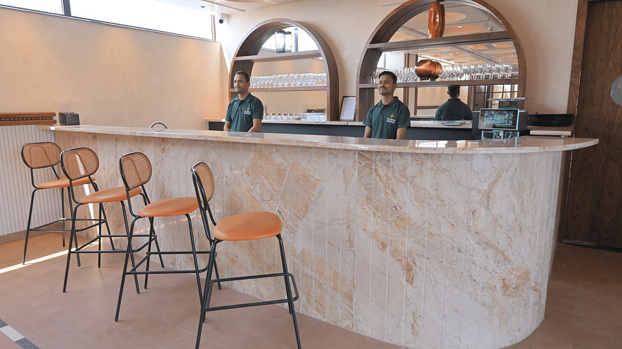 An indoor bar area with a marble counter and several bar stools, with employees standing behind the counter. - Clarks Safari Haridwar